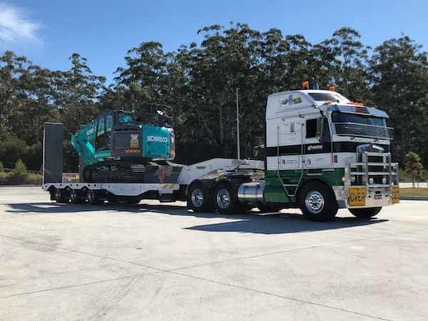 white truck hauling blue excavator