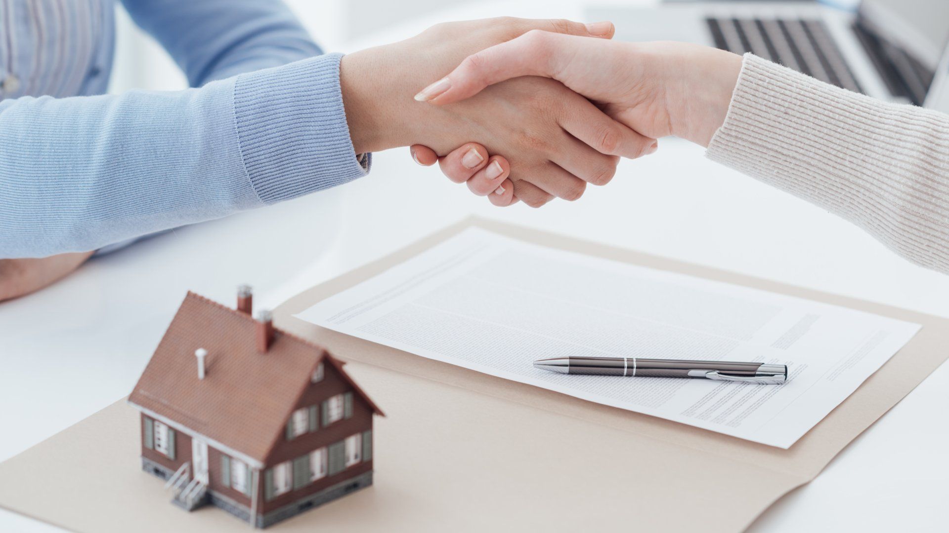 Two people shaking hands over a mortgage contract