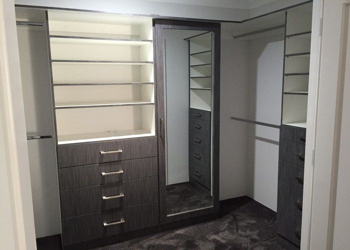 walk in wardrobe with dark brown shelving and tall mirror