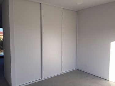 corner of room with white sliding wardrobe and wall