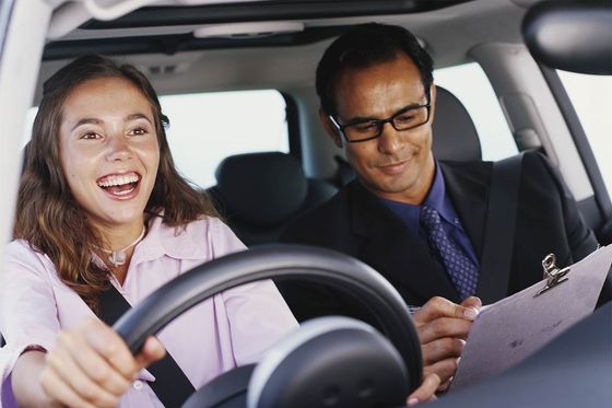 girl driving car smiling and guy with clipboard